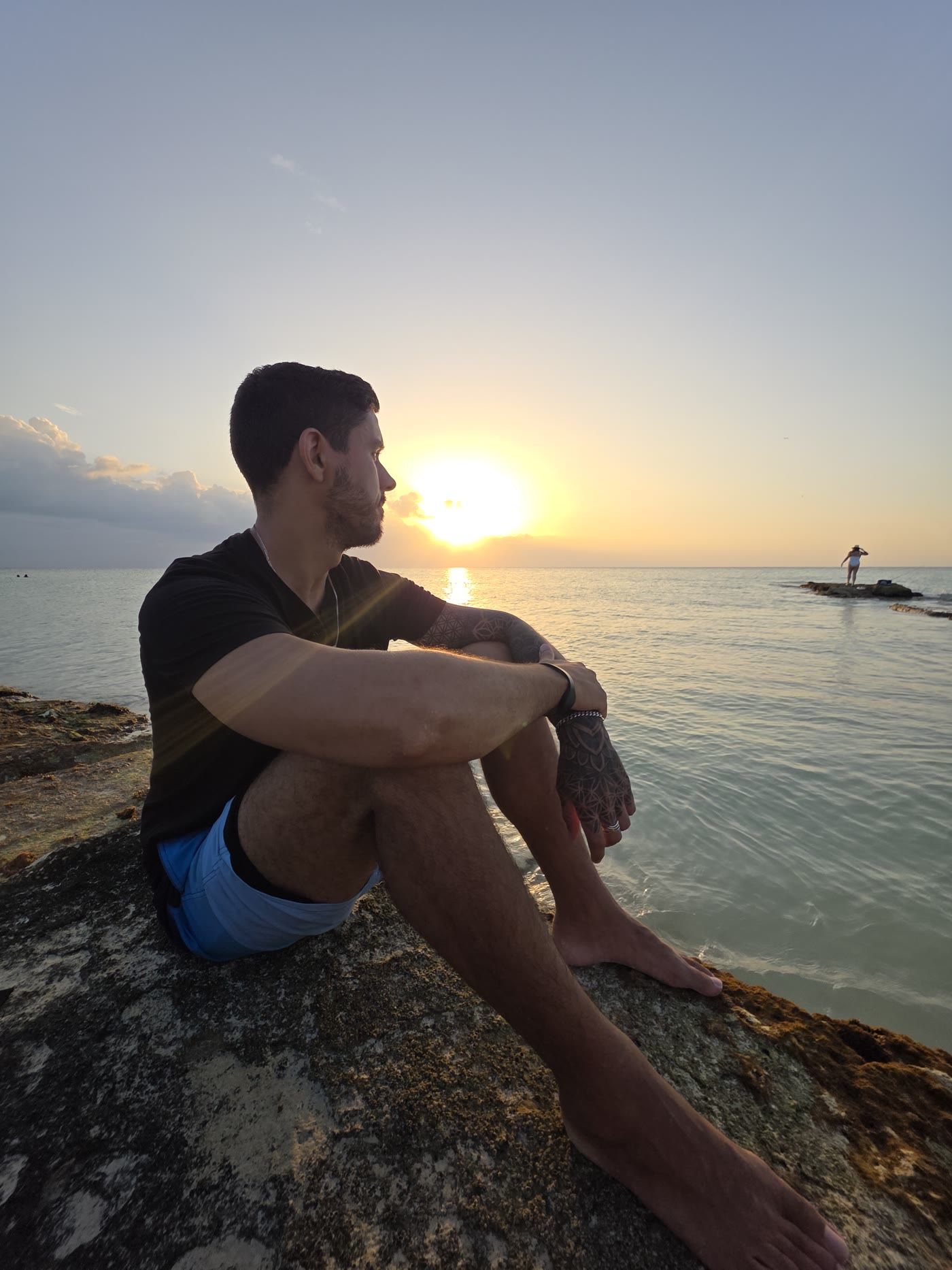 Devin sitting on rocks by the sea at sunset, looking toward the sun